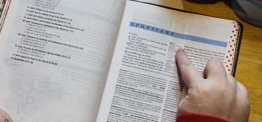 A hand pointing to where the cross references are in a Bible.